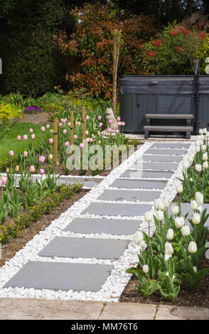 Symphonie verglaste Pflastersteine Form einen Weg zu einem Whirlpool mit Tulipa 'Pink Diamond' und Tulipa 'Kokette' entweder Seite. Credits: Design von Zinn Stockfoto