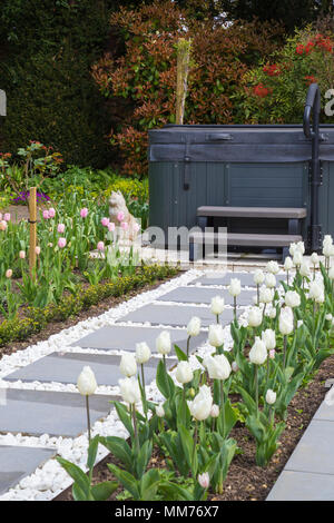 Symphonie verglaste Pflastersteine Form einen Weg zu einem Whirlpool mit Tulipa 'Pink Diamond' und Tulipa 'Kokette' entweder Seite. Credits: Design von Zinn Stockfoto