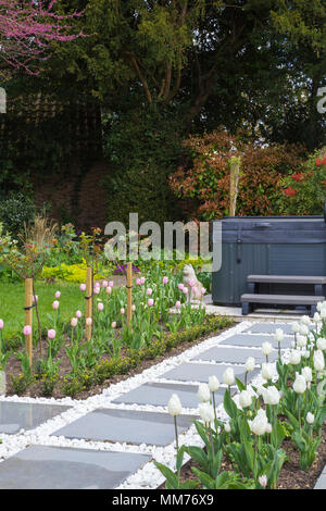 Symphonie verglaste Pflastersteine Form einen Weg zu einem Whirlpool mit Tulipa 'Pink Diamond' und Tulipa 'Kokette' entweder Seite. Credits: Design von Zinn Stockfoto