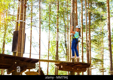 Teenager-Mädchen geht auf aufklappbaren Spuren in extremen Seil Park im Sommer Wald. Höhentraining Klettern Kindes dran Adventure – ausgestattet mit sa Stockfoto