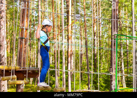 Teenager-Mädchen geht auf aufklappbaren Spuren in extremen Seil Park im Sommer Wald. Höhentraining Klettern Kindes dran Adventure – ausgestattet mit sa Stockfoto