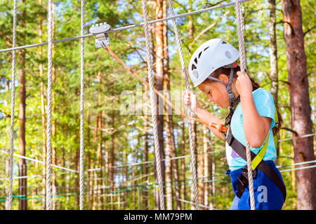 Teenager-Mädchen geht auf aufklappbaren Spuren in extremen Seil Park im Sommer Wald. Höhentraining Klettern Kindes dran Adventure – ausgestattet mit sa Stockfoto