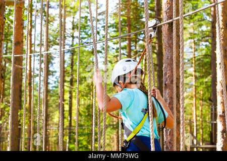 Teenager-Mädchen geht auf aufklappbaren Spuren in extremen Seil Park im Sommer Wald. Höhentraining Klettern Kindes dran Adventure – ausgestattet mit sa Stockfoto