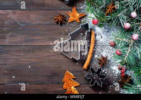 Spicy Christmas background zum Backen, Formulare für Cookies, Orangeat, Zimtstangen, Sternanis, Tanne auf dem alten dunklen Hintergrund. Ansicht von oben, kopieren Stockfoto