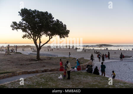 Gruppen von Menschen auf einem Strand in Camps Bay bei einem schönen Sonnenuntergang in Kapstadt, Südafrika Stockfoto