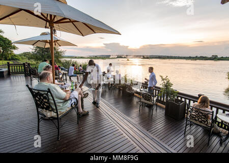Eine Gruppe von Hotel die Gäste des Royal Livingstone Hotel auf der Sonnenterrasse sitzen und den Sonnenuntergang über dem Sambesi Livingstone, Sambia beobachten Stockfoto