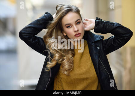 Blonde Frau im städtischen Hintergrund. Schöne junge Mädchen mit schwarzen leder jacke und mini rock auf der Straße stand. Hübsche Russische Frauen mit Stockfoto