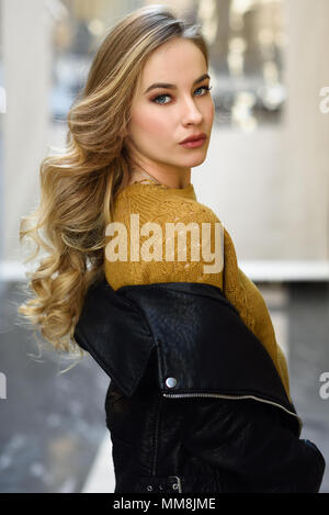 Blonde Frau im städtischen Hintergrund. Schöne junge Mädchen mit schwarzen leder jacke und mini rock auf der Straße stand. Hübsche Russische Frauen mit Stockfoto