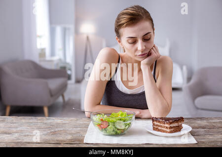 Nachdenkliche junge Frau am Kuchen suchen Stockfoto