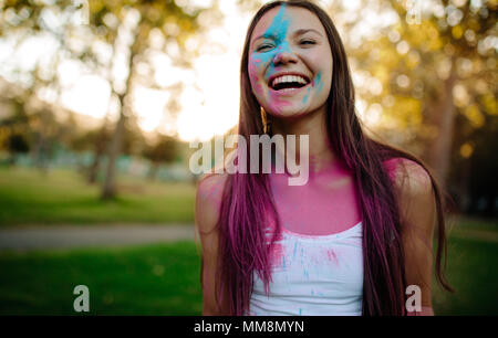 Schöne Frau mit farbigem Pulver auf ihrem Gesicht verschmiert. Lächelnde Mädchen spielen mit Farben während des Holi Festival im Park. Stockfoto