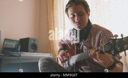 Junge attraktive männliche Musiker komponiert und Datensätze soundtrack Gitarre spielen mit Computer, auf Gesicht und Hände konzentrieren Stockfoto