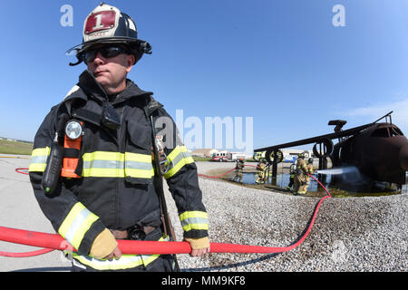 Ein 72Nd Bauingenieur Squadron Feuerwehrmann dazu neigt, eine rote Hand - Schlauch während einer Schulungsveranstaltung im Full-size Flugzeugbrand Trainingsgerät auf dem Flugplatz entfernt Sept. 13, 2017, Tinker Air Force Base, Oklahoma. Feuerwehrmänner von Tinker AFB wurden von den Mitgliedern der Internationalen Flughafen Tulsa Feuerwehr während der jährlichen Rezertifizierung verbunden. (U.S. Air Force Foto/Greg L. Davis) Stockfoto