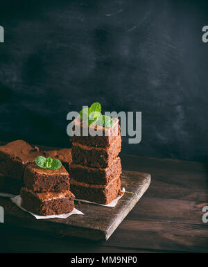 Zwei Stapel von quadratischen Stücke Schokolade gebackene brownie Torte auf einem braunen Holzbrett, Vintage, Tonisierung, Kopie Raum