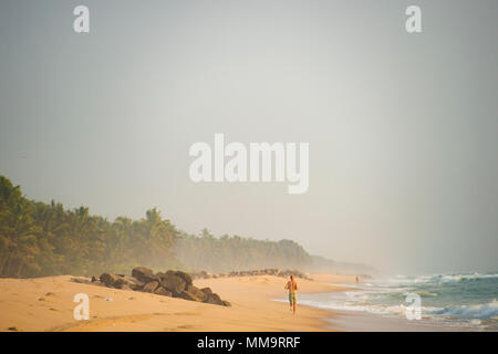 Ein Mann in einem Badeanzug läuft am Strand bei Sonnenuntergang. Varkala tropischen Strand, Kerala, Indien. Stockfoto