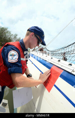 Petty Officer 2nd class David Nelson, ein Maschinen Techniker mit der Coast Guard Golf Strike Team, Orte eine Bewertung Aufkleber auf dem Rumpf eines Schiffes durch Hurrikan Irma im Boot Key Hafen, in der Nähe von Marathon, Florida, Sept. 29, 2017 verdrängt. Weitere Informationen für Schiffseigner daran interessiert, ihr Boot entfernen bei Http://myfwc.com/boating/vessel-hotline/removal/. U.S. Coast Guard Foto von Petty Officer 2. Klasse David Weydert. Stockfoto