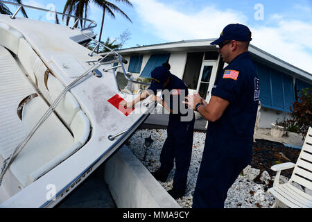 Lt. j.g. Samantha Cardoza und Petty Officer 1st Class Brian Moehler, Mitglieder der Atlantischen Strike Team in Fort Dix, New Jersey befindet, bringt eine Bewertung Aufkleber auf der Rumpf eines vertriebenen Schiff in einen Kanal auf Sugarloaf Key, Florida, Oktober 2, 2017. Bewertet Schiffe sind für Ausbau auf ihre Bedrohung für die Umwelt und ihre Gefahr zur Navigation priorisiert. U.S. Coast Guard video von Petty Officer 2. Klasse David Weydert. Stockfoto