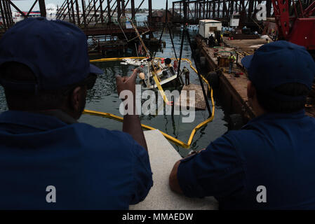 Feuerwehrmann Zeon Johnson (links) und Petty Officer 3rd Class Zach Wenig, ein Marine science Techniker (rechts), überwachen die Erholung Der arbeitsboot König Triton, Donnerstag, Oktober 5, 2017, im Hafen von Boston. Das Paar überwacht auf Anzeichen von Verschmutzung und gewährleistet, dass risikogerechte Auffangvorrichtungen und saugfähig Boom rund um König Triton, der an seinem Liegeplatz zwei Tage zuvor gesunken bereitgestellt wurde. (U.S. Coast Guard Foto von Petty Officer 3. Klasse Andrew Barresi) Stockfoto