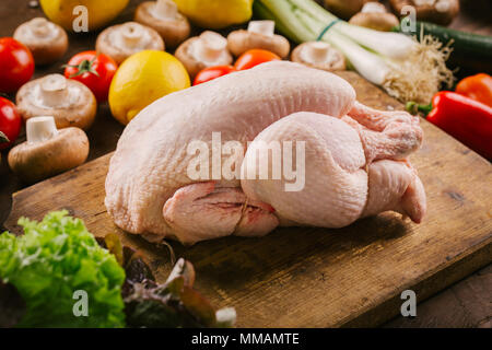 Nahaufnahme des Ganzen rohem Huhn auf alten Vintage Schneidbrett mit frischem Gemüse der Saison. Stockfoto