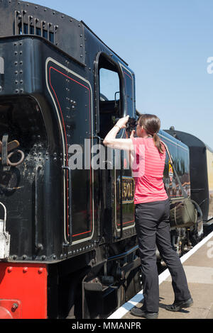 Weibliche Zug enthusiast Fotografieren von glänzenden aufgeregt, haltbar, Dampflok, stationär auf der Plattform, auf einem herrlich sonnigen Morgen im Mai. Stockfoto