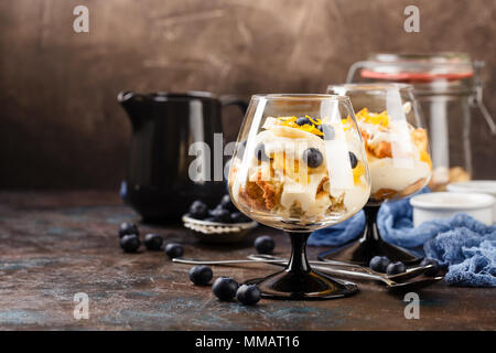 Gesunde hausgemachte layered Dessert trifle mit Orange, Heidelbeere, Keksen, Joghurt und Müsli in einem Gläser Stockfoto