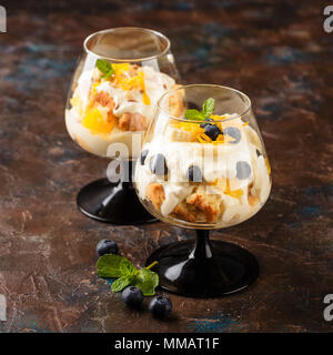 Zwei Gläser mit Gesunden hausgemachte layered Dessert trifle mit Orange, Heidelbeere, Keksen, Joghurt und Müsli Stockfoto