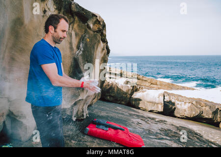 Junge Kletterer mann Beschichtung seine Hände in Pulver chalk Magnesium für das Klettern an der Küste Stockfoto