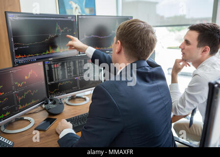 Handel mit Aktien Online-Unternehmer. Börsenmakler Blick auf Grafiken, Indizes und Zahlen auf mehrere Computer-Bildschirme. Kollegen in der Diskussion Trad. Stockfoto