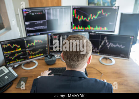 Blick über die Schulter des Geschäftsmannes trading Stocks. Lager Händler Suche in Graphen, Indizes, Zahlen und Analysen auf mehreren Bildschirmen in m Stockfoto