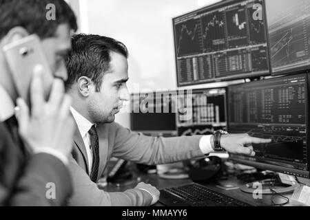 Handel mit Aktien Online-Unternehmer. Börsenmakler Blick auf Grafiken, Indizes und Zahlen auf mehrere Computer-Bildschirme. Kollegen in der Diskussion Trad. Stockfoto
