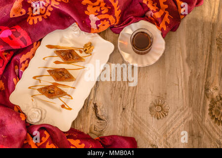 Obere Ansicht geschossen von traditionellen aserbaidschanischen Baklava mit Nussbaum und Tee in Ceramic White Platte über rustikal Tischplatte. Horizontale Komposition. Cop Stockfoto