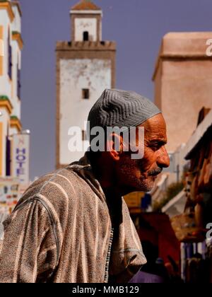 Nahaufnahme eines marokkanischen Mannes in traditioneller Kleidung, der am Turm der Moschee in Essaouira, Marokko, vorbeigeht Stockfoto