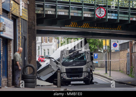 Eine Garage Arbeiter aus einem MoT Testing Center und die beschädigten Nachwirkungen des Lkw an der Universität Loughborough Junction, nachdem es in einem Der eisenbahnbrücken - ein wichtiger Transportweg für Pendler in die Stadt stürzte, am 8. Mai 2018, im Süden von London, England. Wurde eine Person verletzt. Stockfoto