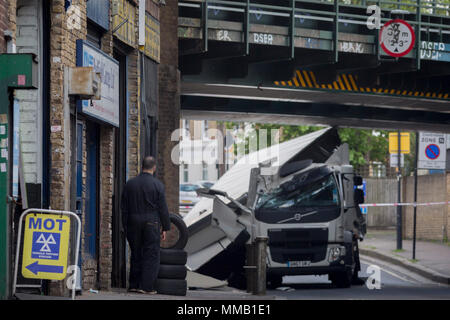 Eine Garage Arbeiter aus einem MoT Testing Center und die beschädigten Nachwirkungen des Lkw an der Universität Loughborough Junction, nachdem es in einem Der eisenbahnbrücken - ein wichtiger Transportweg für Pendler in die Stadt stürzte, am 8. Mai 2018, im Süden von London, England. Wurde eine Person verletzt. Stockfoto