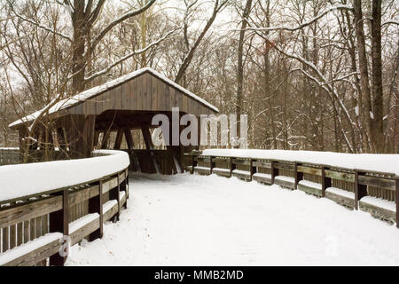 Winter Szene mit einer Wicklung Holzsteg führt zu einer überdachten Brücke, ein Fluss in einem bewaldeten Park kreuzt. Stockfoto