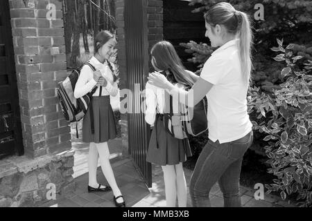 Schwarz-weiß-Bild der jungen Mutter helfen Tochter zur Schule Taschen setzen Stockfoto