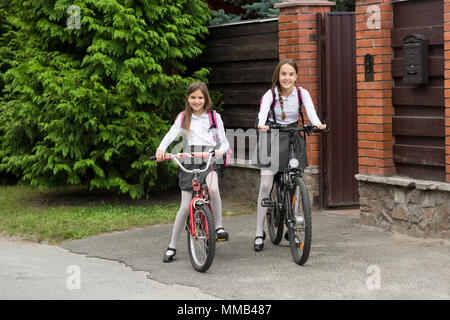 Zwei lächelnde Mädchen in Schuluniform reiten auf Fahrrädern zur Schule Stockfoto