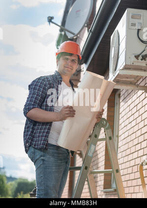 Portrait von jungen männlichen Techniker stehen auf trittleiter mit Blueprints Stockfoto