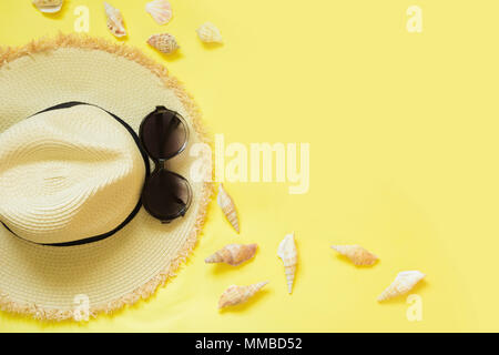 Stroh's Beach foman Hut und schwarzer Sonnenbrille mit Muscheln auf gelben Hintergrund. Ansicht von oben. Flach. Stockfoto