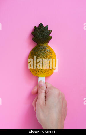Hand mit Ananas popsicle auf rosa Hintergrund. Ansicht von oben Stockfoto
