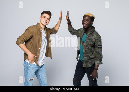 Kaukasische Mann, der Hohe fünf seiner afrikanischen Freund über grauen Hintergrund. Stockfoto
