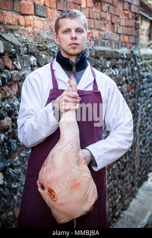 Junger Mann mit Schürze stehen im Freien, Schinken, bei Kamera schaut. Stockfoto