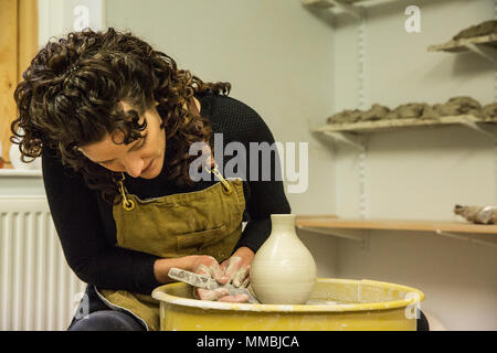 Frau mit braunen lockigen Haar zu tragen Schürze Gestaltung Ton Vase auf Keramik Rad. Stockfoto