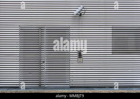 Äußere Videoüberwachungs- und Sicherheitssystem mit CCTV-Kamera auf einem Wellblech Wand über den Eingang des Gebäudes zu sehen. Stockfoto