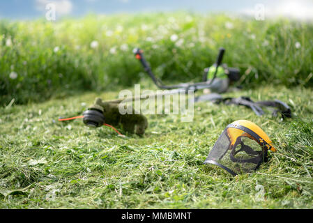 String Trimmer und schützende Maske auf gemähten Gras, Gras und den blauen Himmel im Hintergrund Stockfoto