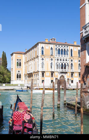 Gondoliere entspannen in seine Gondeln auf dem Canal Grande mit dem Palazzo Cavalli-Franchetti hinter ihm, Venedig, Venetien, Italien, als er wartet auf Touristen Stockfoto