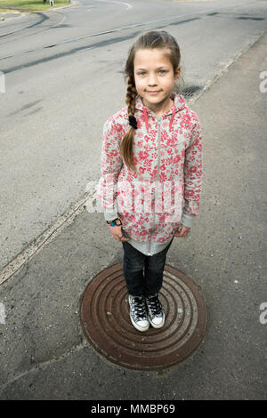 Kind, Mädchen in der Mitte der metallischen Luke stehen auf leere Urban Street Stockfoto