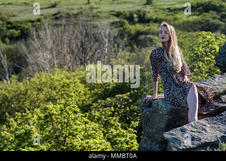 Schöne Mädchen im Kleid sitzt auf Felsen in der Natur Stockfoto