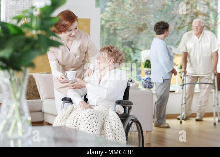 Freundlich Krankenschwester gibt eine Tasse Tee behinderte Frau im Rollstuhl in den älteren Home Stockfoto