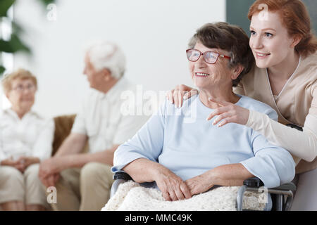 Assistant zeigt, etwas zu den Patienten im Rollstuhl in den älteren Home Stockfoto