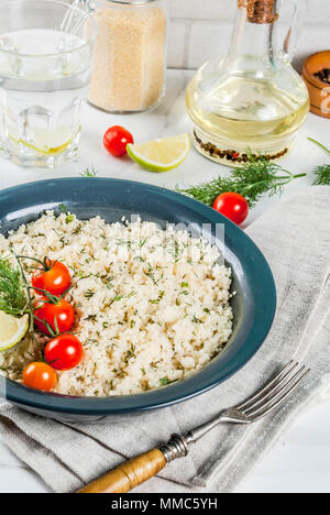 Licht diätetische Lebensmittel, Couscous mit Tomaten, Kalk und frischen Kräutern in dunklen Schale, weißer Marmor Hintergrund Stockfoto